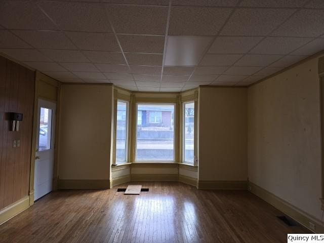 empty room featuring hardwood / wood-style flooring, a paneled ceiling, and a healthy amount of sunlight