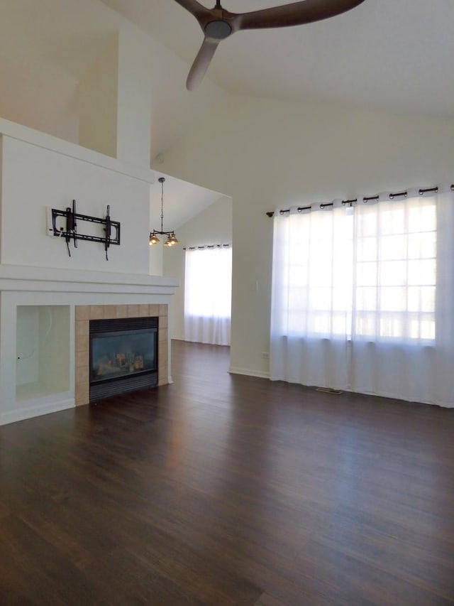 unfurnished living room with ceiling fan with notable chandelier, dark wood-type flooring, a tile fireplace, and vaulted ceiling