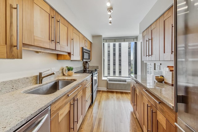 kitchen with light stone countertops, sink, stainless steel appliances, a wall mounted air conditioner, and light wood-type flooring