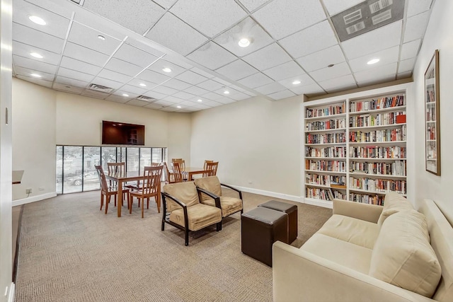 sitting room featuring a paneled ceiling, built in shelves, and light carpet