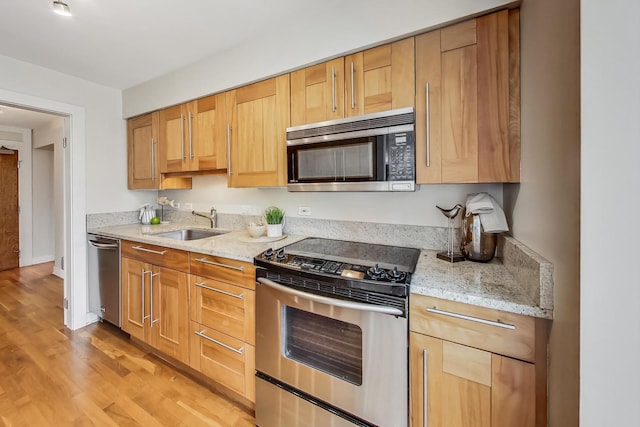 kitchen with light stone counters, sink, stainless steel appliances, and light hardwood / wood-style floors