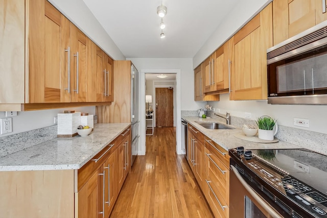 kitchen featuring light stone counters, sink, stainless steel appliances, and light hardwood / wood-style flooring