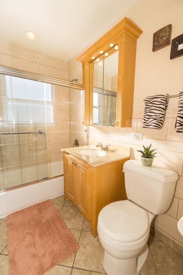 full bathroom featuring toilet, combined bath / shower with glass door, tile walls, tile patterned floors, and vanity