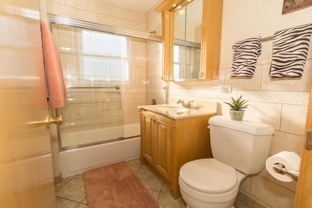 full bathroom featuring tile patterned flooring, toilet, combined bath / shower with glass door, vanity, and tile walls