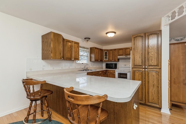 kitchen featuring electric stove, kitchen peninsula, a kitchen bar, sink, and light hardwood / wood-style flooring