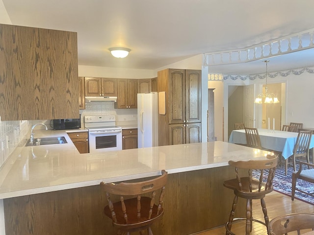 kitchen with kitchen peninsula, a notable chandelier, a kitchen breakfast bar, white appliances, and sink