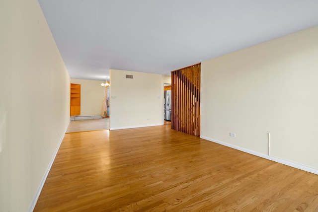 spare room with a baseboard heating unit, an inviting chandelier, and light hardwood / wood-style flooring