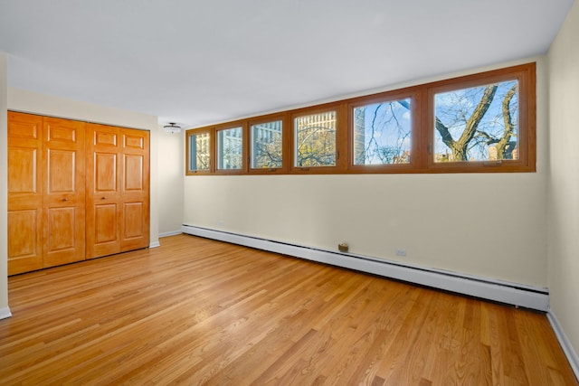 unfurnished bedroom featuring a baseboard heating unit, light wood-type flooring, and a closet