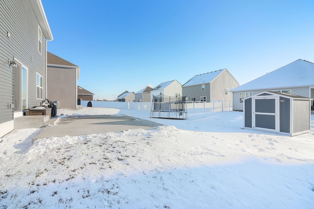 yard covered in snow with a storage unit and a trampoline