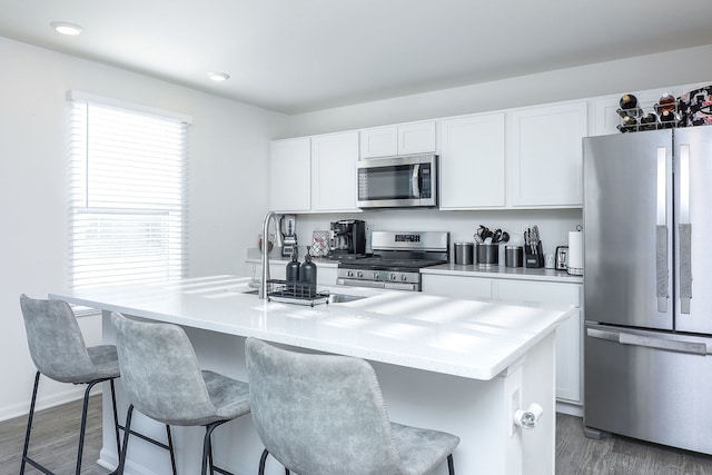 kitchen with dark hardwood / wood-style floors, stainless steel appliances, an island with sink, and white cabinets