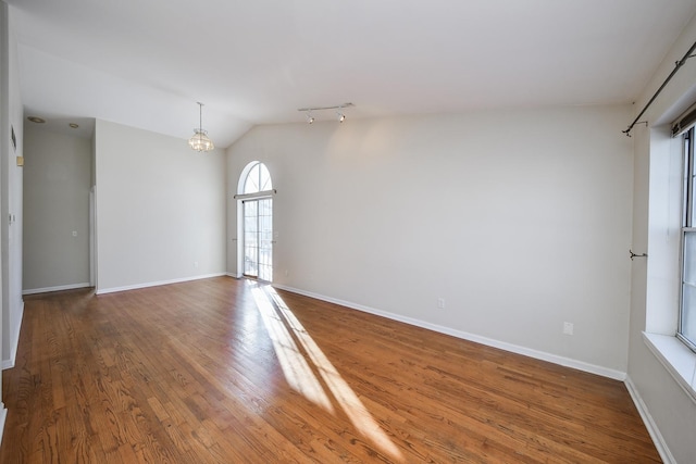 unfurnished room with lofted ceiling, hardwood / wood-style flooring, track lighting, and a chandelier