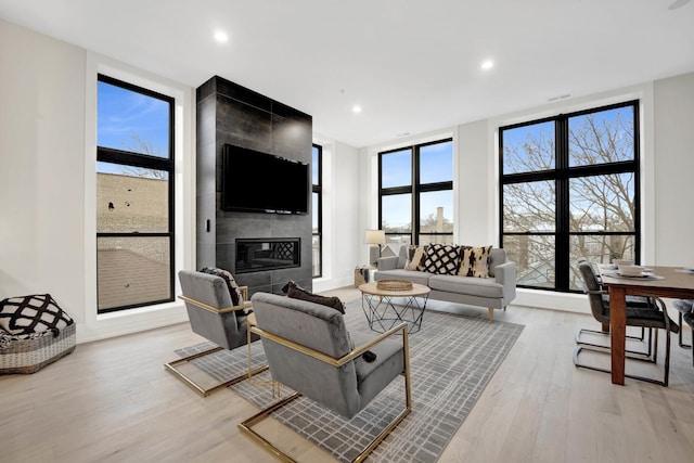 living room with light hardwood / wood-style floors, expansive windows, and a tiled fireplace