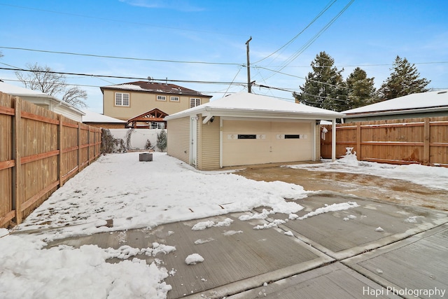 snow covered rear of property with a garage and an outbuilding