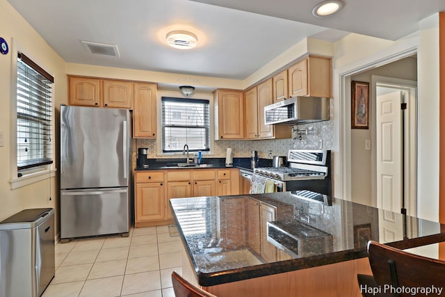 kitchen with a kitchen island, stainless steel appliances, dark stone countertops, backsplash, and light tile patterned floors