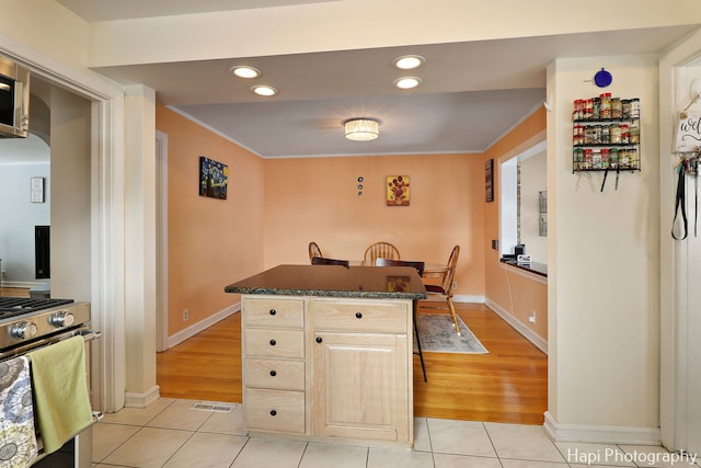 kitchen featuring light tile patterned floors, stainless steel range with gas stovetop, dark stone countertops, and a center island