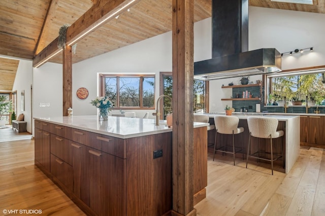 kitchen with a large island, wood ceiling, wall chimney exhaust hood, beamed ceiling, and light wood-type flooring