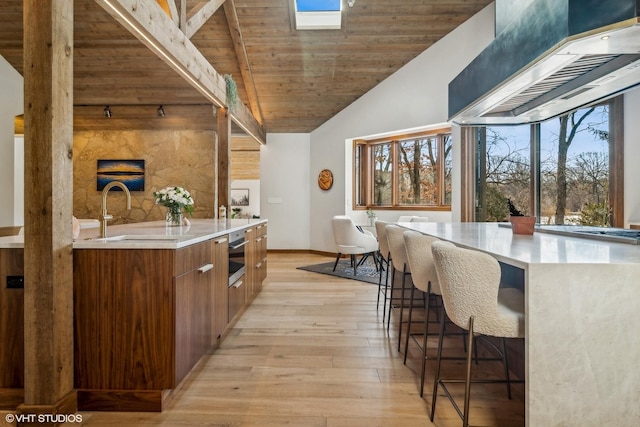 kitchen with sink, wood ceiling, a breakfast bar, stainless steel oven, and light wood-type flooring