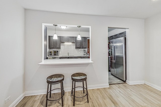 kitchen with light hardwood / wood-style floors, kitchen peninsula, appliances with stainless steel finishes, dark brown cabinets, and a breakfast bar