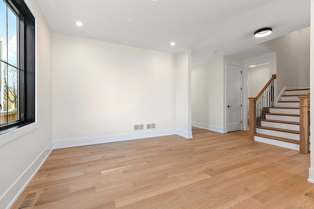 spare room with light wood-type flooring, visible vents, baseboards, and stairs