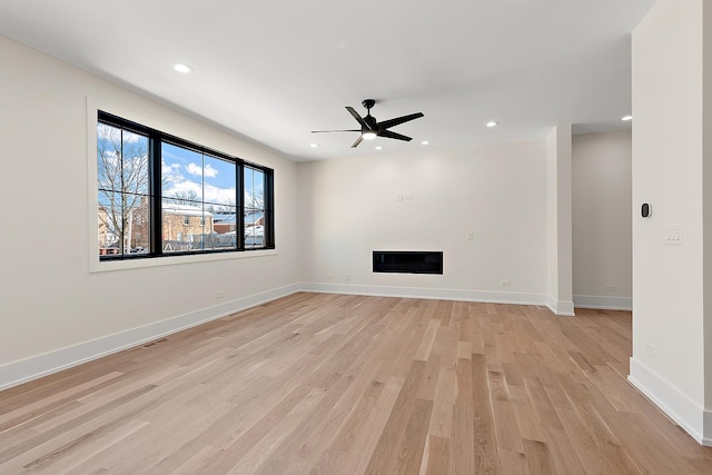 unfurnished living room featuring recessed lighting, a glass covered fireplace, and light wood-style floors