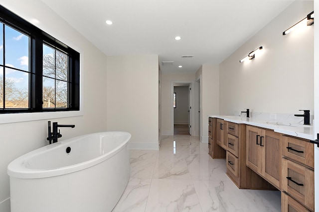 full bathroom featuring marble finish floor, double vanity, recessed lighting, a freestanding bath, and baseboards