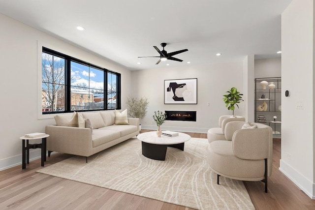 living area with light wood-style floors, a warm lit fireplace, and baseboards