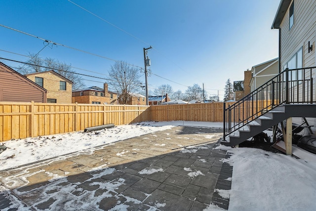 snow covered patio with a fenced backyard, a residential view, and stairway