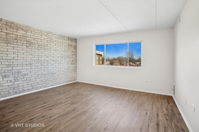 unfurnished room with hardwood / wood-style floors and brick wall