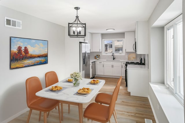 dining room with a notable chandelier, sink, and light wood-type flooring