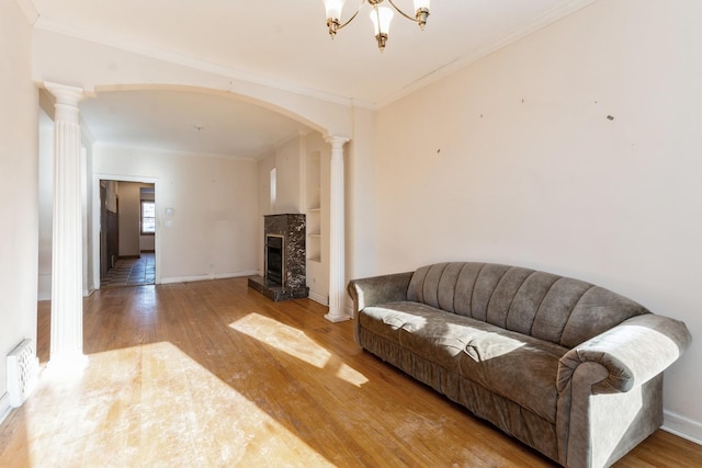 living room featuring a notable chandelier, crown molding, decorative columns, and wood-type flooring