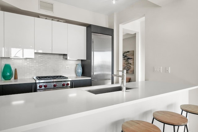 kitchen featuring sink, white cabinets, a kitchen breakfast bar, backsplash, and premium appliances