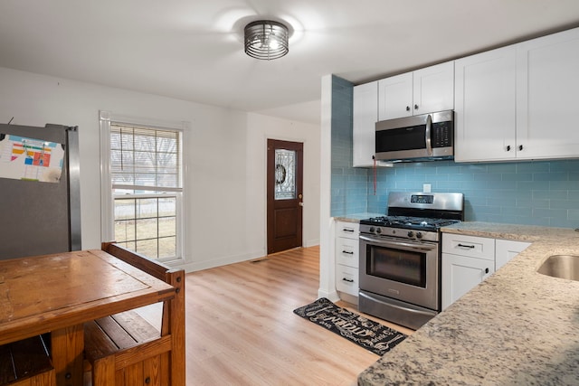 kitchen featuring white cabinetry, stainless steel appliances, tasteful backsplash, light stone countertops, and light wood-type flooring