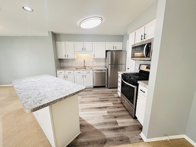 kitchen featuring stainless steel appliances, white cabinetry, a kitchen island, and sink