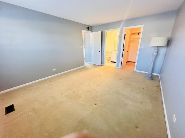 unfurnished bedroom with ensuite bath, light colored carpet, a spacious closet, and a closet