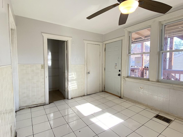 interior space with ceiling fan, a closet, light tile patterned floors, and tile walls