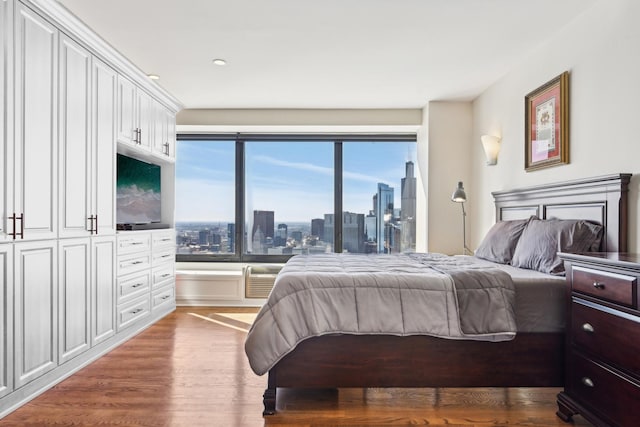 bedroom with access to outside, a wall unit AC, and wood finished floors