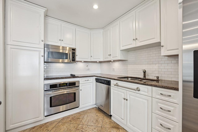 kitchen with a sink, white cabinets, appliances with stainless steel finishes, decorative backsplash, and dark stone counters