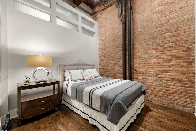 bedroom featuring a high ceiling, wood-type flooring, and brick wall