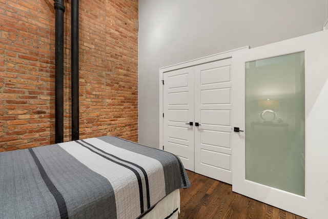 bedroom with dark wood-type flooring, brick wall, and a closet