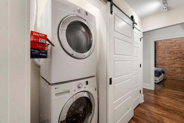 washroom featuring brick wall, stacked washer / drying machine, a barn door, and dark hardwood / wood-style flooring