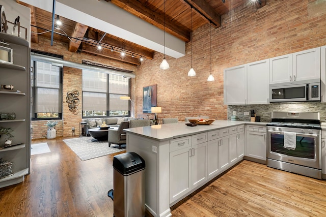 kitchen with pendant lighting, beamed ceiling, stainless steel appliances, and white cabinets