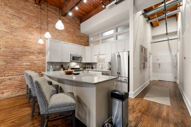 kitchen featuring a towering ceiling, white cabinetry, a breakfast bar area, kitchen peninsula, and stainless steel appliances