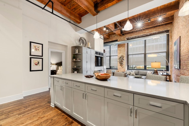 kitchen with pendant lighting, wood ceiling, beam ceiling, brick wall, and light wood-type flooring