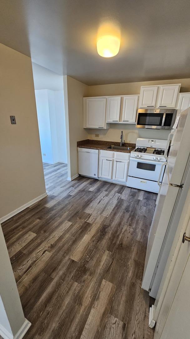 kitchen featuring white appliances, white cabinetry, dark wood-type flooring, and sink