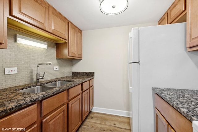 kitchen with light wood-type flooring, dark stone counters, white refrigerator, sink, and backsplash