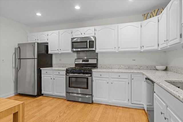 kitchen with appliances with stainless steel finishes, light wood-type flooring, white cabinets, and light stone counters