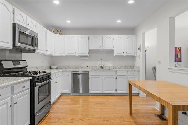 kitchen featuring stainless steel appliances, sink, white cabinets, light stone counters, and light hardwood / wood-style floors