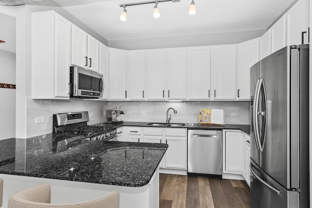 kitchen featuring sink, stainless steel appliances, kitchen peninsula, white cabinets, and dark stone counters