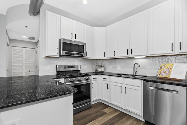 kitchen with sink, dark wood-type flooring, stainless steel appliances, white cabinets, and dark stone counters