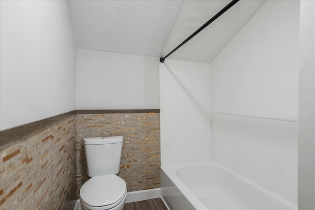 bathroom featuring a washtub, a textured ceiling, hardwood / wood-style floors, toilet, and lofted ceiling